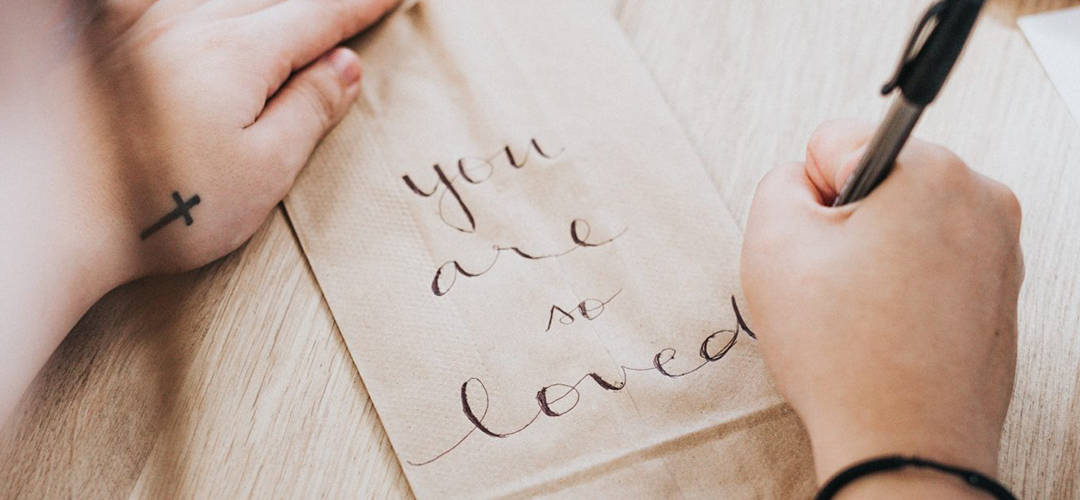 Girl Writing "You are so loved" on a paper bag